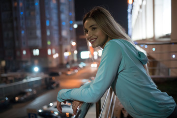 Smiling woman standing on the terrace, night city background