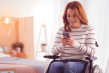 New message. Cheerful mid aged woman using her smartphone while sitting in a wheelchair