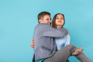 Joking funny couple - girl keeping her boyfriend on her hands over blue background