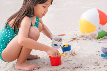 little asian girl playing with sand at the tropical beach in summer.