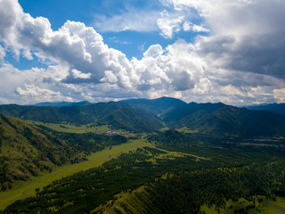 Obraz premium Aerial view to landscape of green valley flooded with light with lush green grass, covered with stone and hills, a fresh summer day under a blue sky with white clouds and sun rays in Altai mountains