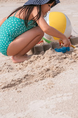 little asian girl playing with sand at the tropical beach in summer.