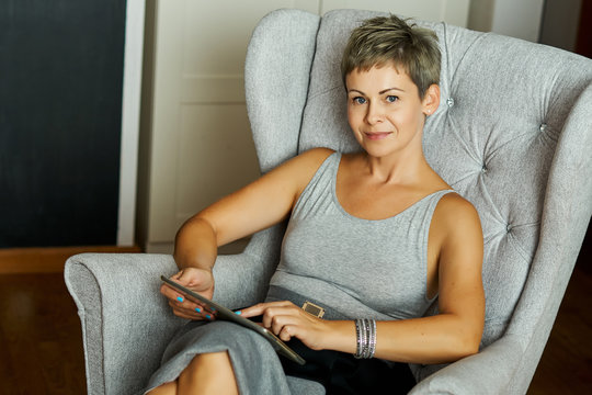 beautiful business woman sitting on a gray chair and works on a tablet at home office