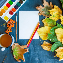 Beautiful autumn leaves, brushes, paint and sheet on a dark background with space for text. Top view, flat layout