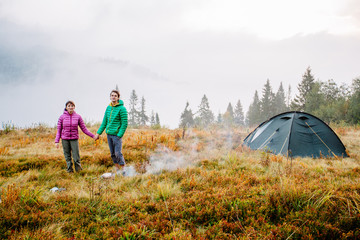 Autumn nature lifestyle happy man and woman relaxing outdoors on camping travel park with frog on background. Hiking couple wearing green and purple down jacket enjoying fall season scenic landscape.