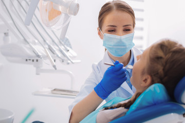 Dental mirror. Careful calm orthodontist checking the condition of jaws while holding a dental...