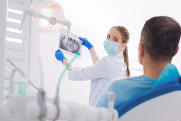 Careful examination. Careful professional dentist putting an X ray image up while showing it to her attentive patient