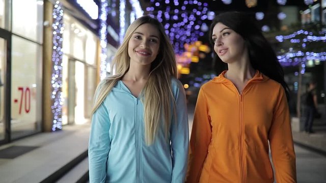Young women friends walking and talking in night city street