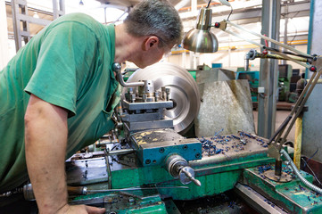 Fototapeta na wymiar The worker, the man, makes mechanical actions of the machine control. Turning work in production.