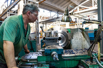 Worker, a man processes metal products on a machine. Turning work in production.