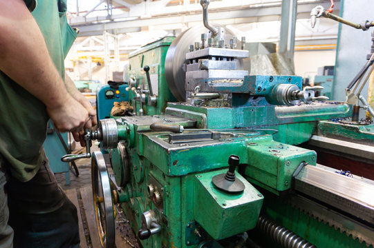 The worker, the man, makes mechanical actions of the machine control. Turning work in production.