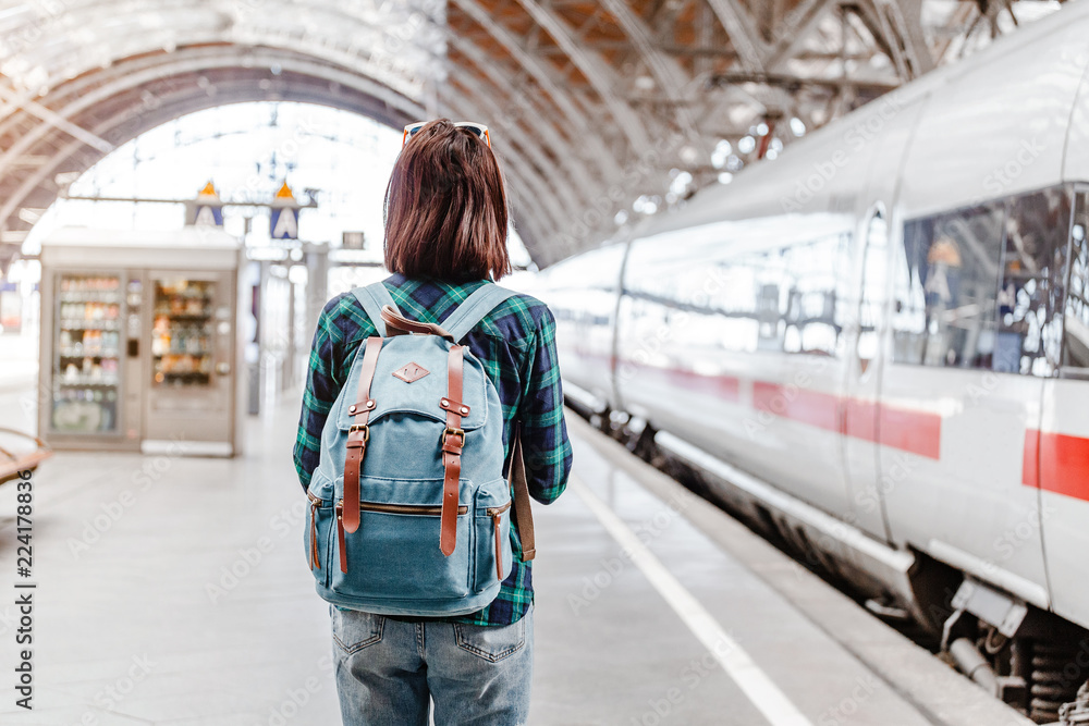 Wall mural a young tourist girl with backpack waits for train on railway station