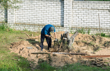 man with an ax uproots a tree stump on a summer day