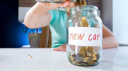 Closeup photo of young woman filling moneybox for purchasing new car with golden coins