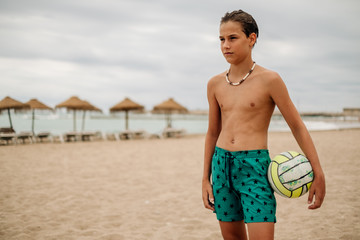 Fototapeta na wymiar Wet boy holding volleyball ball on the beach
