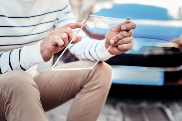 Want to use it. Modern man keeping gadget in both hands and leaning arms on knees while sitting near his auto