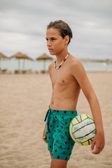Angry wet boy holding volleyball ball on the beach