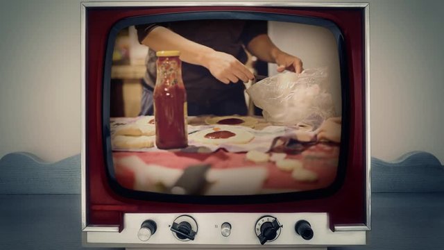 A retro vintage TV showing a little girl and her mother cooking panzerotti (detail of the hands). The table is filled with dough, tomato juice and mozzarella cheese.
