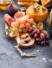 Cheese plate served with grapes, jam, figs, crackers and nuts on a grey background. Copy space.