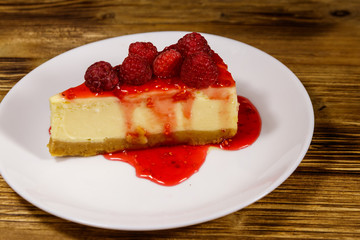 Piece of tasty New York cheesecake with raspberries and raspberry jam in a white plate on wooden table