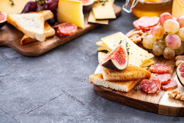 Cheese plate served with grapes, jam, figs, honey, crackers and nuts on a grey background. Copy space.