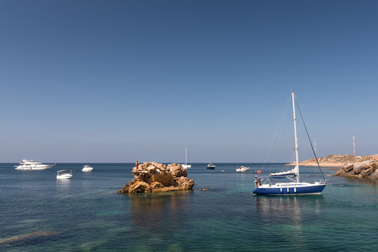 
A yacht and other small boats, floating on a clear, aqua marine sea, off the coast of southern Spain in the summer.  