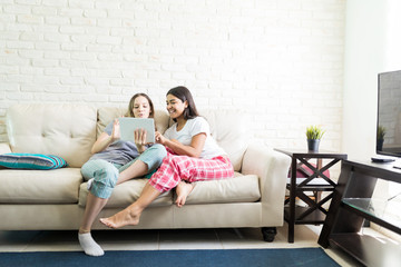 Females In Pajamas Using Digital Tablet While Relaxing On Sofa