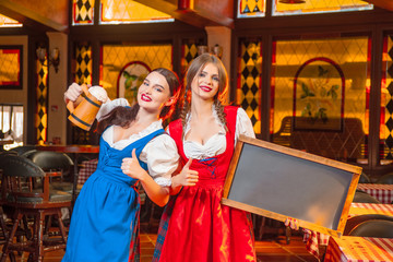 Young girls with wooden beer mugs and a wooden tablet for text in hands at the Oktoberfest festival.