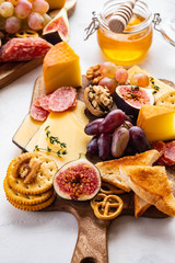 Cheese plate served with grapes, jam, figs, crackers and nuts on a white background. Copy space.
