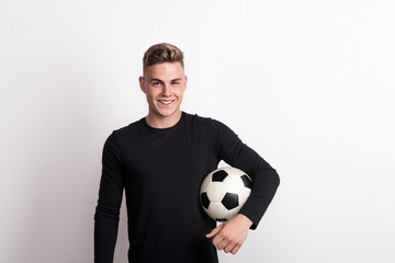 Portrait of a young man with football ball in a studio. Copy space.