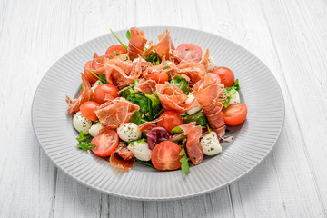 Salad with fresh vegetables with dried tomatoes, meat and mustard, mozzarella, prosciutto
