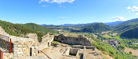 Obraz premium A landscape of cultivated fields, dense forest and mountains as seen from the ruins of the abandoned castle in the rural medieval town of Boltaña, in the Spanish Aragonese Pyrenees
