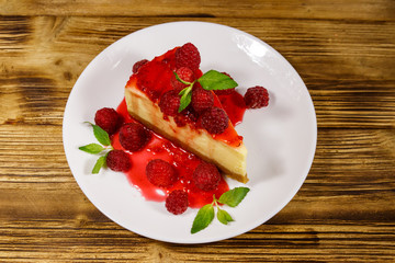 Piece of tasty New York cheesecake with raspberries and raspberry jam in a white plate on wooden table