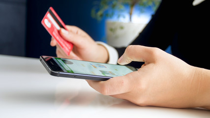 Closeup image of young woman paying with credit card for order in online shop she made on smartphone