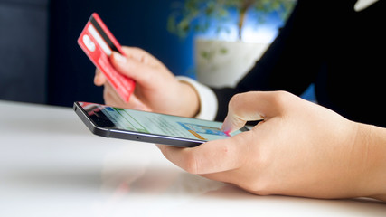 Closeup image of young woman browsing online shop on smartphone and holding credit card