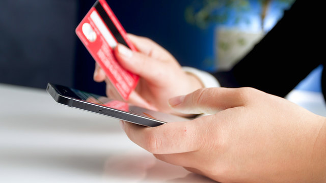 Closeup image of young woman making online purchases with credit card and smartphone