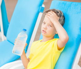 Little boy on the beach with a sunstroke touches his forehead, checking the temperature