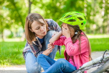 Mother puts a bandage on a wound to little girl, who fell off his bicycle