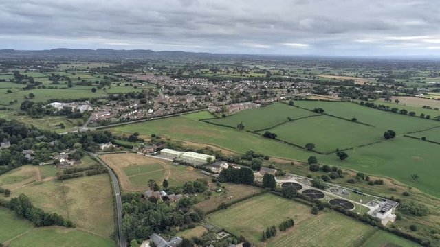 Aerial view, zoom out move. Sewage works, Tarvin residential area houses among fields on Cheshire countryside.