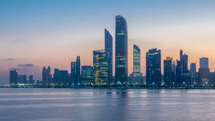 Selbstklebende Fototapete Abu Dhabi Abu Dhabi city skyline with skyscrapers before sunrise with water reflection night to day timelapse