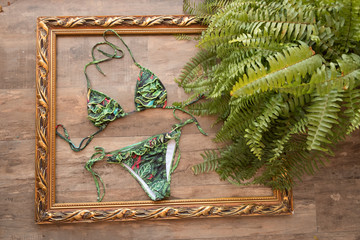 Bikini suit, green palm leaves arranged on wooden background. Summer holidays vacation concept.