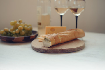 white wine,green gpapes in the plate,slaced cheese and baguette on the cutting board/ 