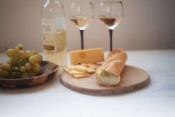 white wine,green gpapes in the plate,slaced cheese and baguette on the cutting board/ 