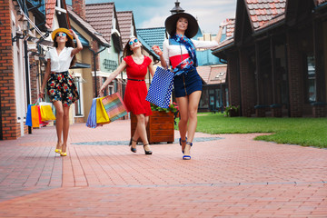 Pretty happy bright women female girls friends in colorful dresses, hats and high heels with shopping bags walking at street after shopping in shopping mall in summer. Shop sales, black Friday.