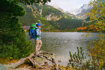 Beautiful young woman with big tourist backpack wearing blue outdoor jacket and knitted hat near...