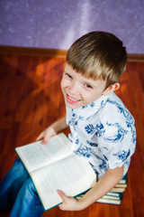 Little boy in a light shirt sits with a book in his hands and smiles