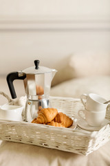 Fototapeta na wymiar Breakfast in bed. On a white wicker tray there is a coffee maker, coffee white cups and croissants.