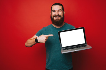 Smiling bearded man pointing at white laptop screen, copyspace