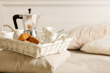 Breakfast in bed. On a white wicker tray there is a coffee maker, coffee white cups and croissants.