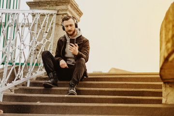 A handsome young hipster man sitting on the stairs and taking a selfie with his smartphone.